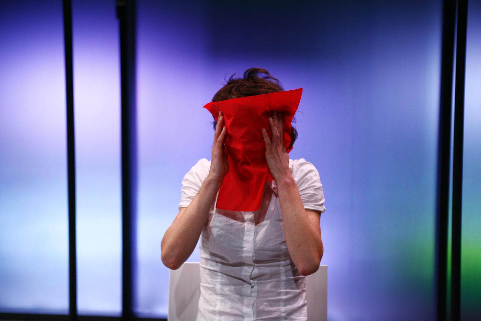 Un visage masqué par un tissu rouge devant des parois bleues