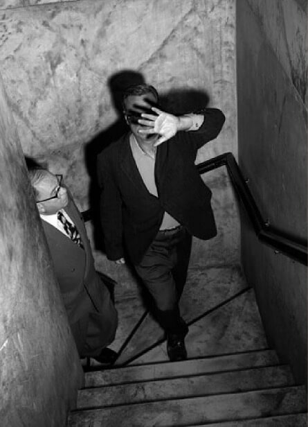 Homme dans un escalier protégeant son visage face à un photographe